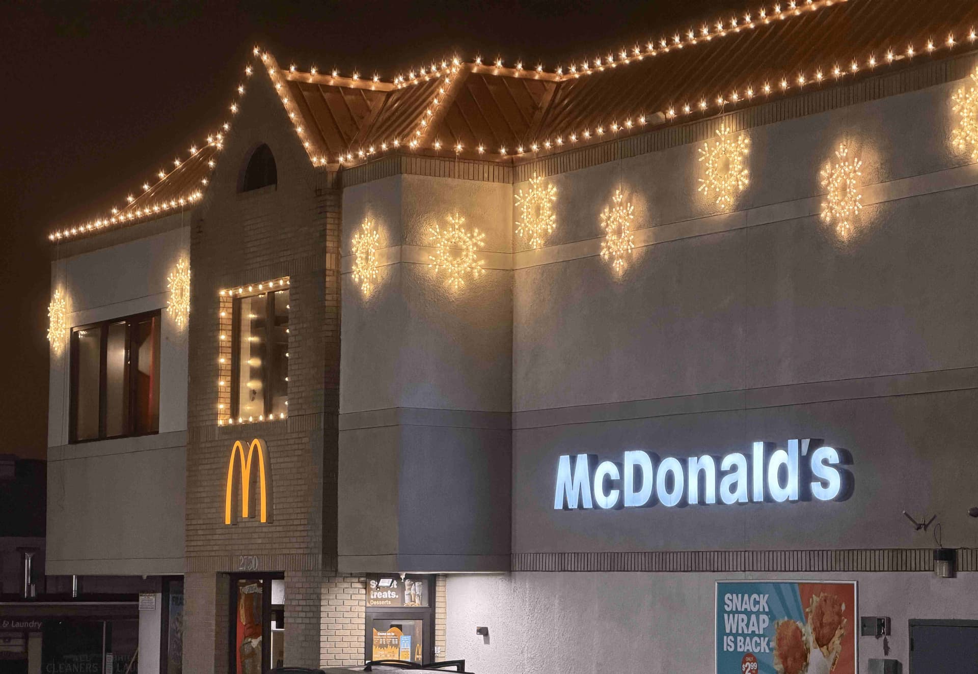 McDonald's restaurant exterior at night with warm white roofline Christmas lights and snowflake medallions