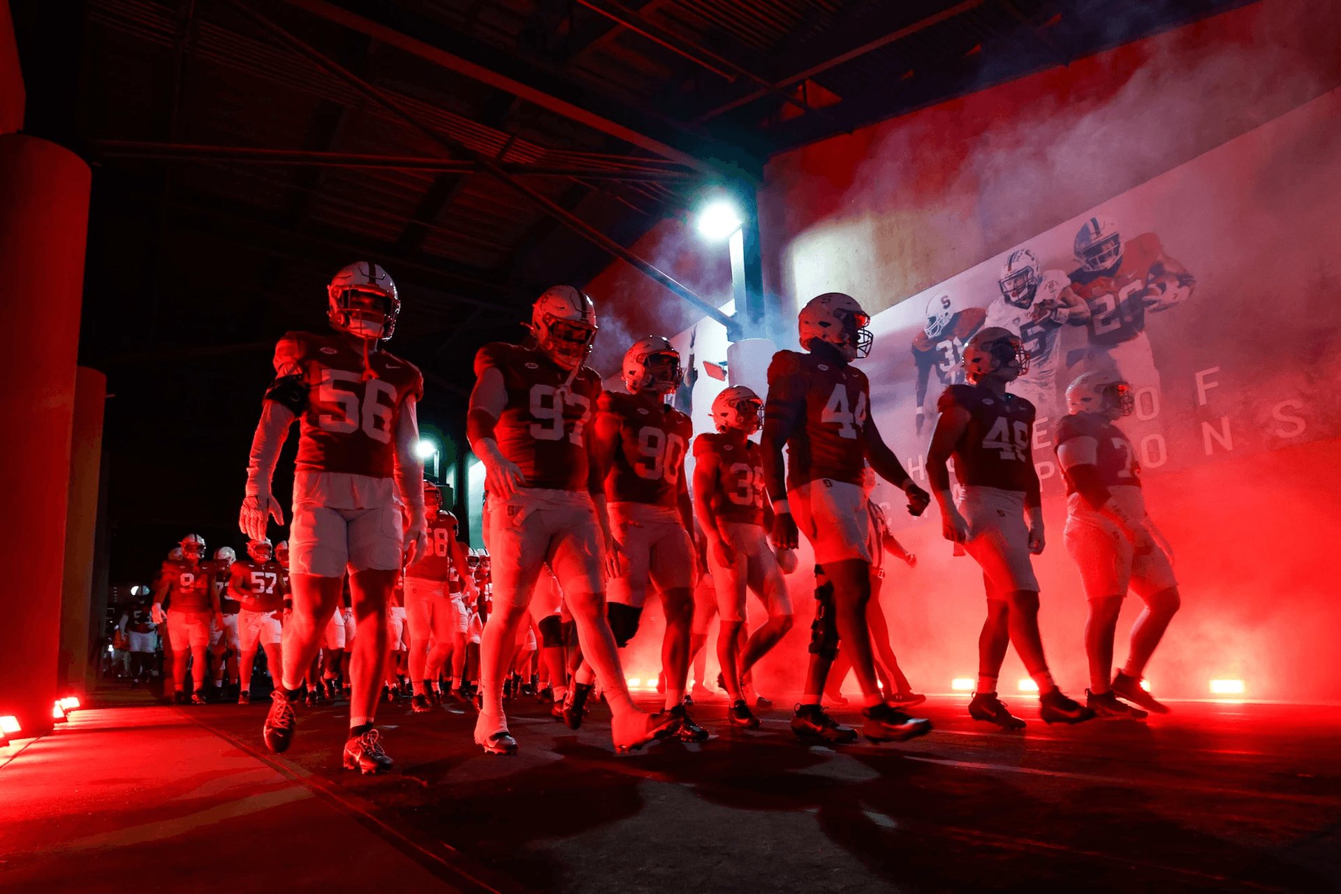 Stanford football team walking out of a dramatically lit stadium tunnel with red lighting and smoke effects