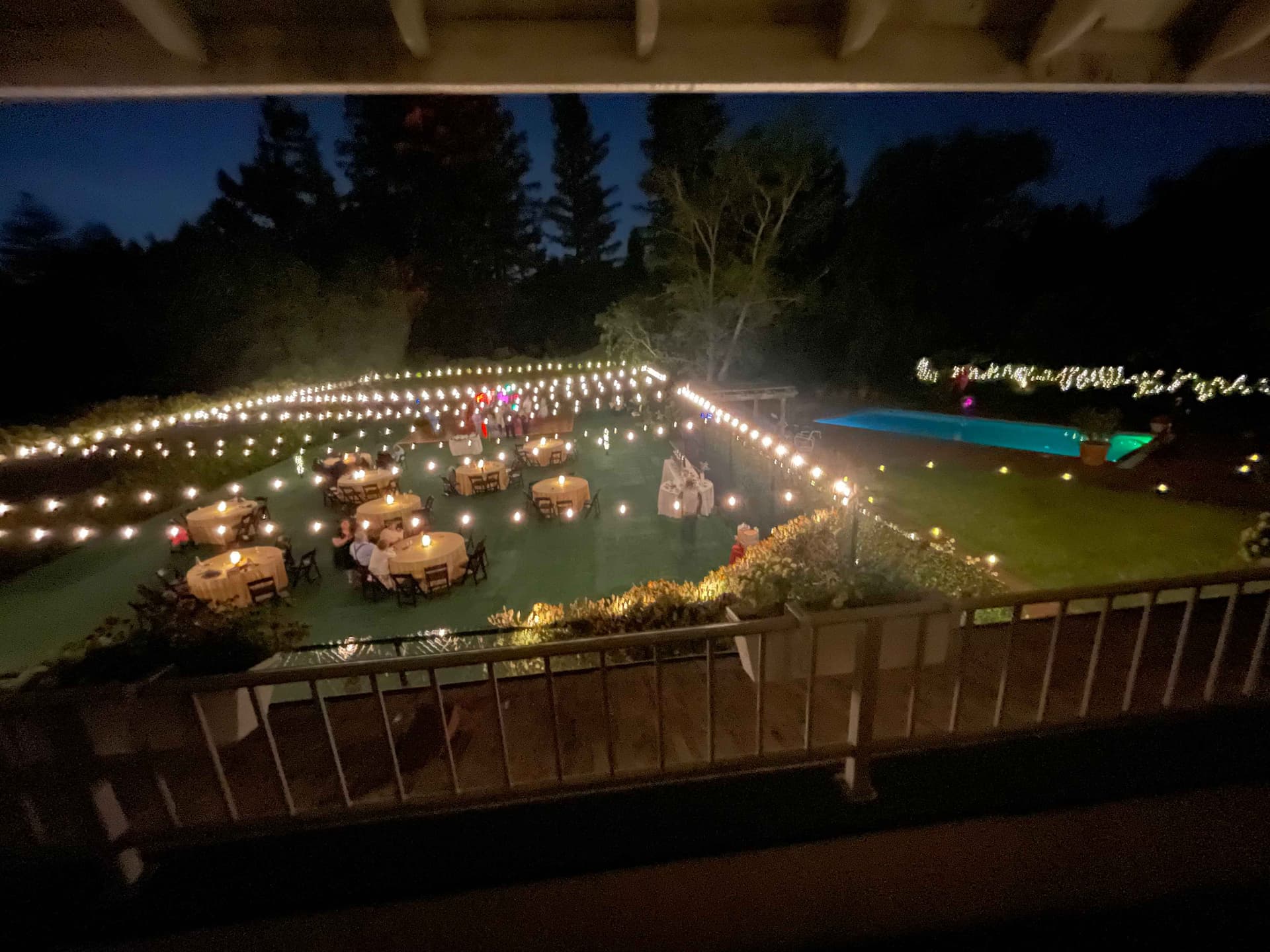 Overhead view of a large estate reception with globe stake lights across the lawn and a lit pool
