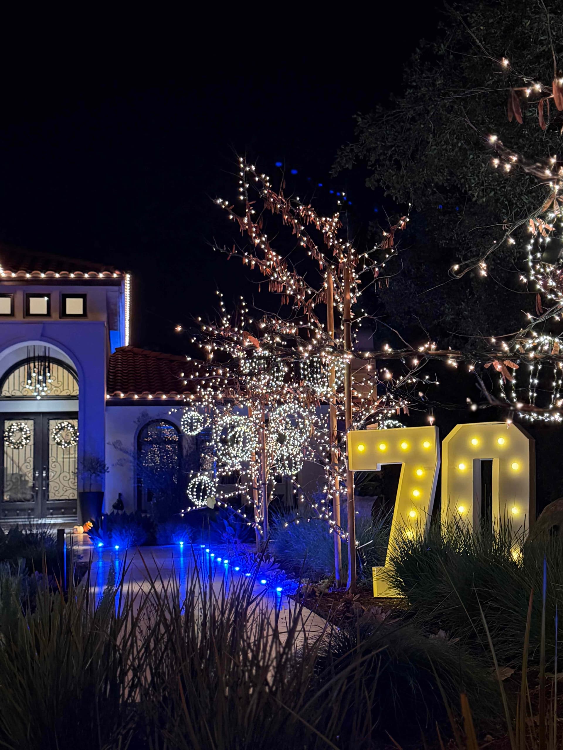 Densely wrapped trees with blue uplighting and marquee letters for a milestone birthday