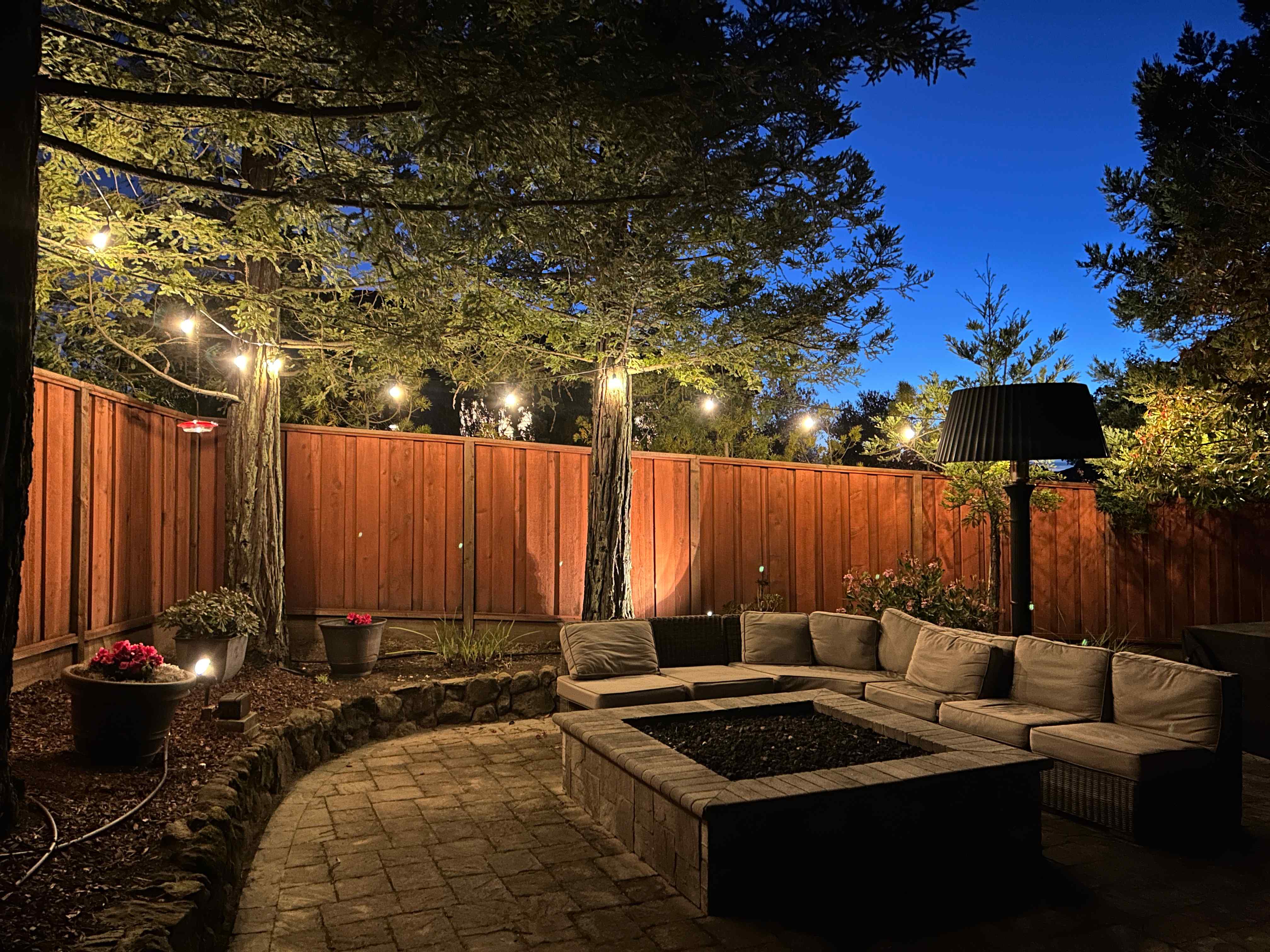 Cozy outdoor lounge area with string lights in trees and comfortable seating around fire pit