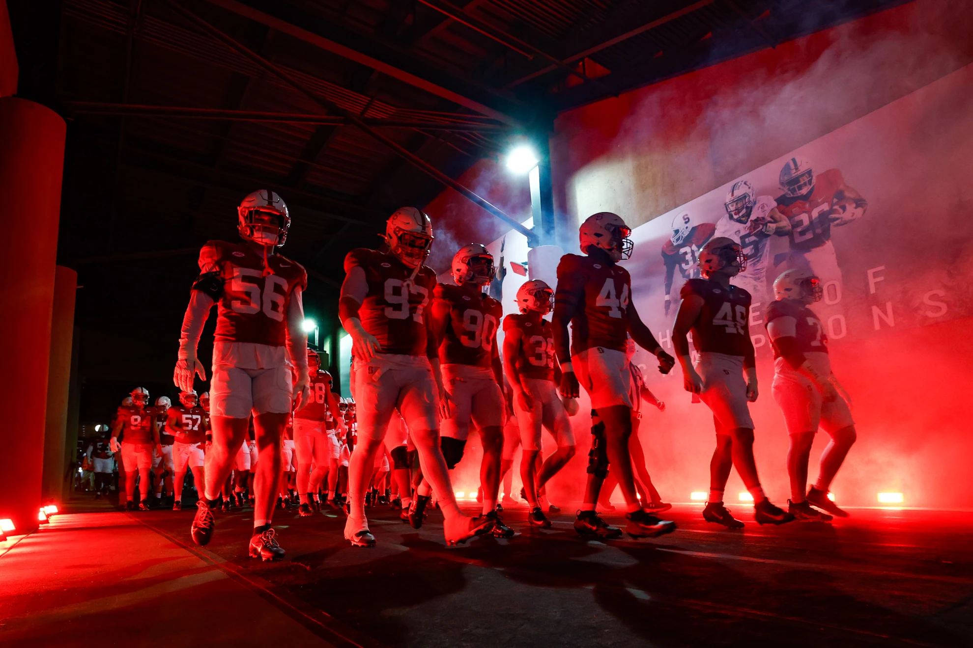 Stanford football team walking out of a dramatically lit stadium tunnel with red lighting and smoke effects